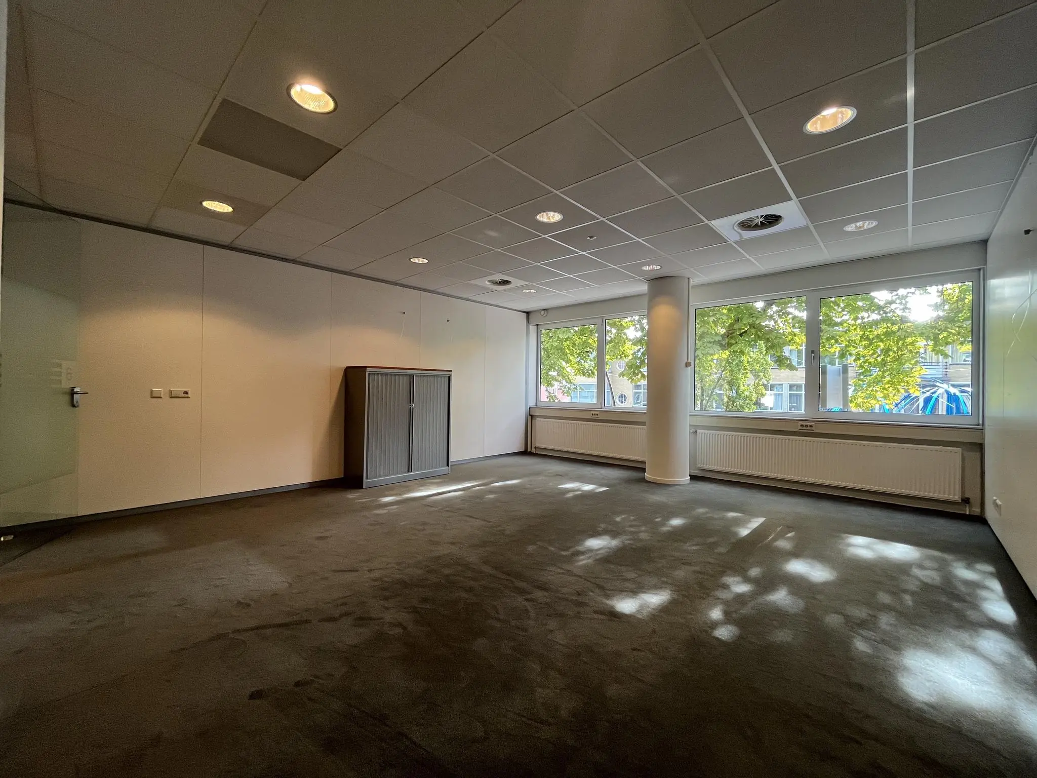 Licht en leeg kantoorruimte aan de 1e Hogeweg met grote ramen en uitzicht op bomen.